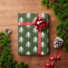 a present wrapped in green wrapping paper with white trees on it, surrounded by christmas decorations and pine cones