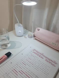 a desk with a notebook, pen and glasses on it next to a glass of water