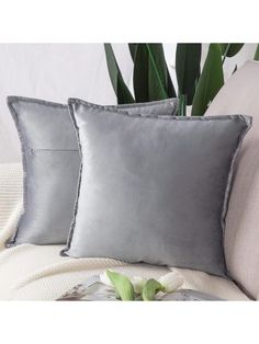 two silver pillows sitting on top of a couch next to a vase with green plants