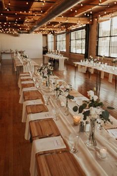 long tables with white linens and centerpieces are lined up in an empty room