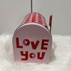 a red and white tin can with the words love you on it sitting on a fluffy surface