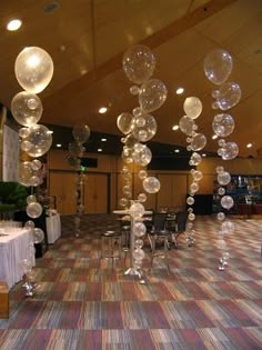 a room filled with tables covered in white tablecloths and balloons hanging from the ceiling