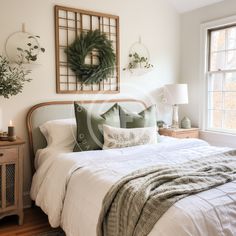 a bed with white sheets and pillows in a bedroom next to a window filled with greenery