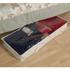 an open storage box on the floor in front of a bed with blankets and pillows