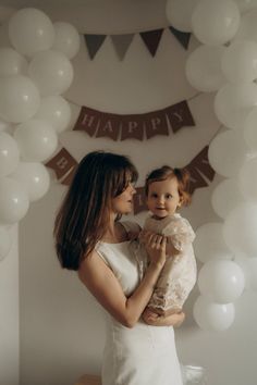 a woman holding a small child in her arms while standing next to balloons and bunting