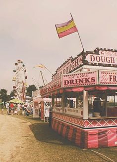 an old photo of a carnival booth with flags flying in the wind and people walking around