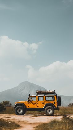 a yellow jeep is parked on the side of a dirt road with mountains in the background