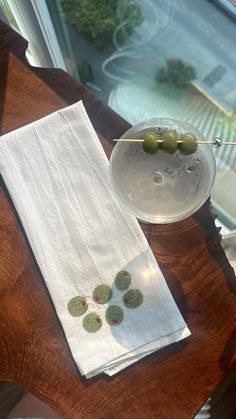 a wooden table topped with a glass bowl filled with olives next to a white towel