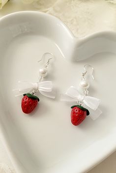 a pair of earrings with a strawberry on it sitting on a heart shaped plate next to flowers