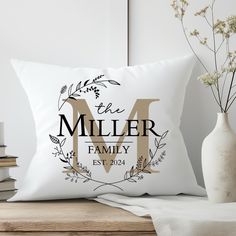 a white pillow with the letter m on it next to some books and a vase