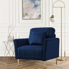 a blue chair in a white room with a gold floor lamp and painting on the wall