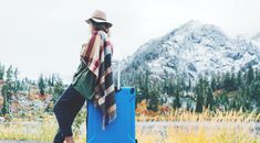 a woman sitting on top of a blue suitcase in front of a snow covered mountain