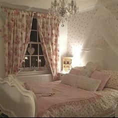 a white bed sitting in a bedroom next to a window with pink curtains and pillows