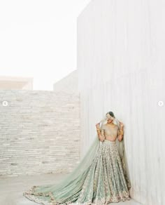 a woman in a wedding dress leaning against a wall with her back to the camera