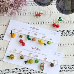 some fruit earrings are sitting on top of a piece of paper next to two wine glasses