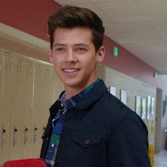 a young man standing in a hallway holding a red case and smiling at the camera