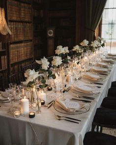 a long table is set with white flowers and candles for an elegant wedding reception in the library