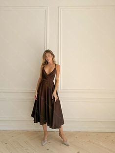 a woman standing in front of a white wall wearing a brown dress and silver shoes