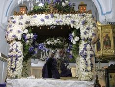 a priest standing in front of a white and blue floral alter with flowers on it