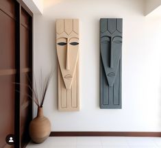 two wooden sculptures are on the wall next to a vase