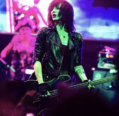 a woman with long hair and piercings playing bass guitar in front of an audience