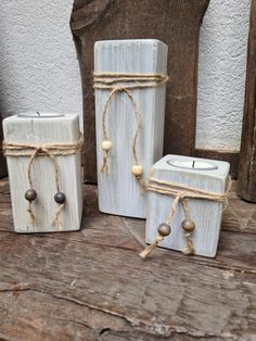 three white candles are sitting on a wooden table and tied with twine, one candle is in the shape of a rectangle