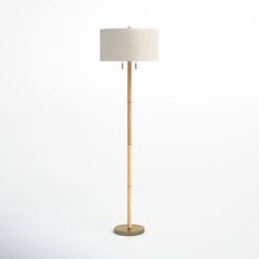 a wooden floor lamp with a white shade on the base and a beige fabric lampshade