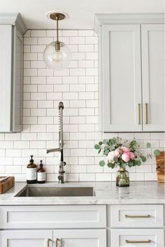 a white kitchen with marble counter tops and brass pulls on the faucet above the sink