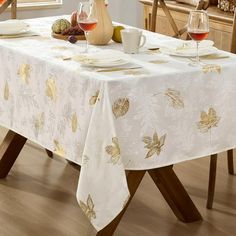 a dining room table with white and gold leaves on the table cloth, wine glasses, and plates