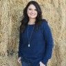 a woman standing in front of a hay bale with her hands in her pockets