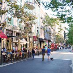 people are walking down the street with umbrellas on either side and tables in front of them