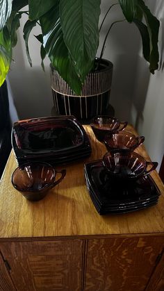 a wooden table topped with lots of black plates and bowls next to a potted plant