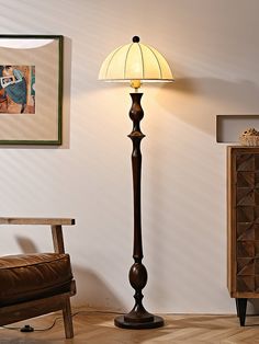 a lamp that is sitting next to a chair in a room with pictures on the wall