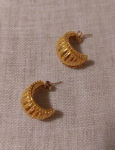 In the British Museum, there is a  small collection of gold earrings from the Temple of Artemis at Ephesus. This pair of earrings is based off a single surviving earring from the seventh century BC.  (650-600 BC). These beautiful crescent earrings depict granulation.  They are nine tenths of an inch long.  Made by the British Museum in conjunction with the Metropolitan Museum of Art.  They are gold over pewter with 14K gold posts. To see the original artifact visit: https://www.britishmuseum.org/collection/object/G_1907-1201-94 Gold Semi-circle Earrings For Gift, Gold Crescent Huggie Earrings, Elegant Gold Semi-circle Earrings, Gold Crescent Huggie Earrings For Gift, Handmade Semi-circle Gold Jewelry, Gold Semi-circle Metal Earrings, Handmade Gold Brass Huggie Earrings, Handmade Gold Huggie Earrings In Brass, Yellow Gold Semi-circle Earrings For Gift