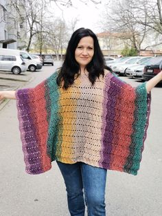 a woman is standing in the street with her arms out and wearing a multicolored crocheted shawl