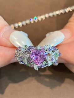 a woman's hand holding a ring with purple and green stones