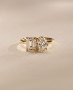 three stone engagement ring with diamond accents in yellow gold and white gold, on a plain surface