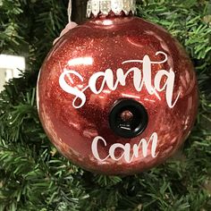 a red ornament with the words santa cam on it hanging from a christmas tree