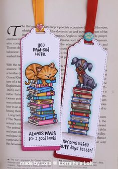 two bookmarks with cats and dogs on them are hanging from a red ribbon in front of an open book