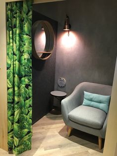 a living room with a chair, mirror and green curtains in the window sill