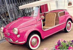 an old pink car parked in front of a building with flowers on the side walk