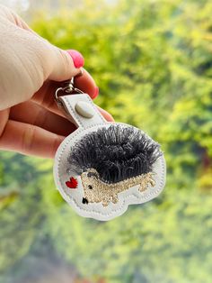 a hand holding a keychain with a small hedgehog on it's side