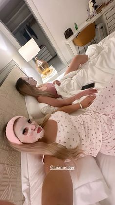 two women laying on a bed wearing pink masks