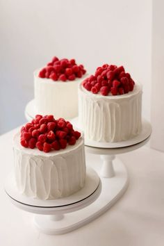 three cakes with white frosting and raspberries on top, one is red