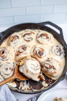 a skillet filled with cinnamon rolls on top of a white counter next to plates