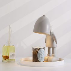 a table with a lamp, candle and some items on it in front of a white wall