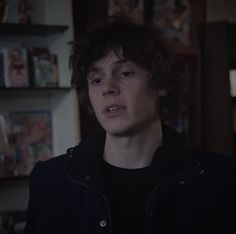 a young man with curly hair standing in front of a bookshelf