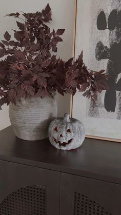 a potted plant sitting on top of a wooden cabinet next to a fake pumpkin