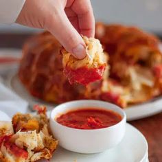 a person dipping sauce onto some food on a white plate with a croissant in the background