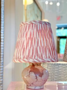 a lamp with a red and white shade on it sitting on a pink table top